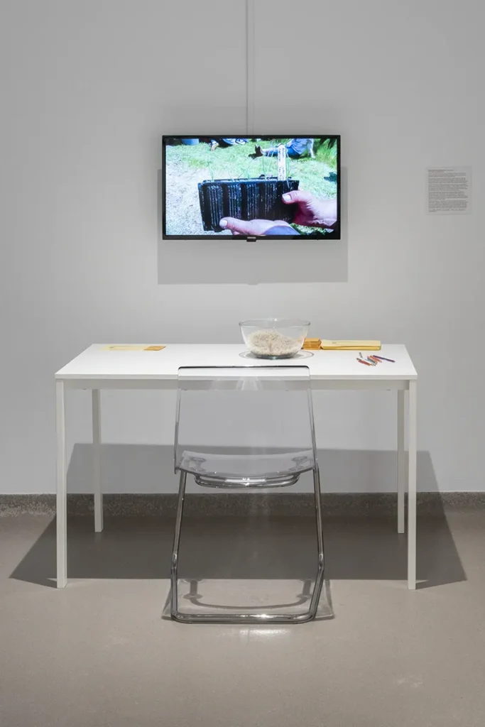 Wall-mounted monitor above a desk and chair, displaying a small planter held in a hand.