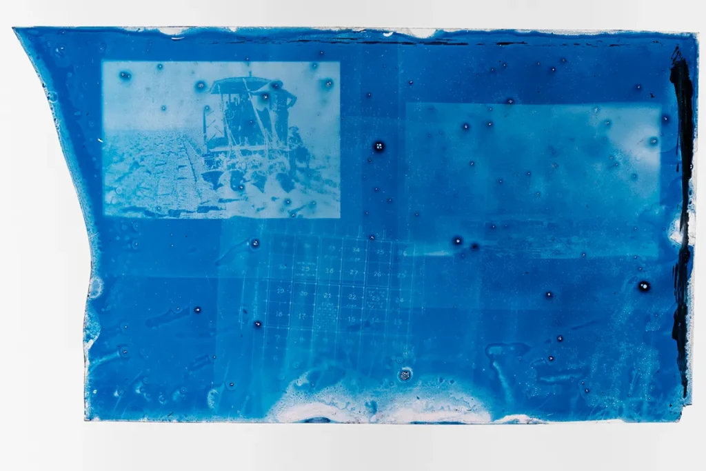 Cyanotype with an image of a farmer beside machinery and a map of land plots.