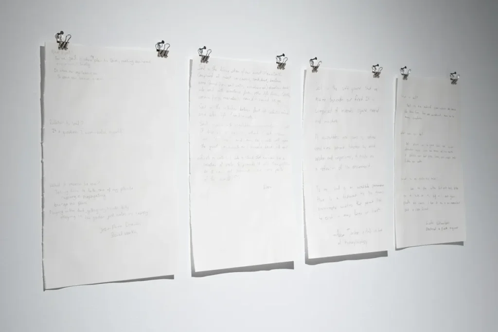 Four sheets of paper with handwritten text mounted on a wall.