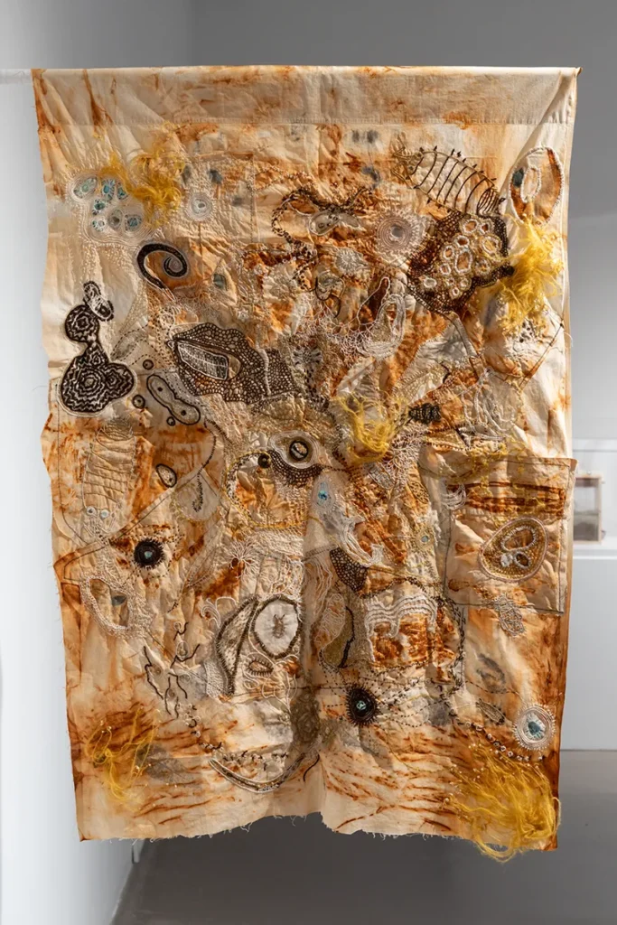 Embroidered and dyed textile hanging from a wall-mounted staff.